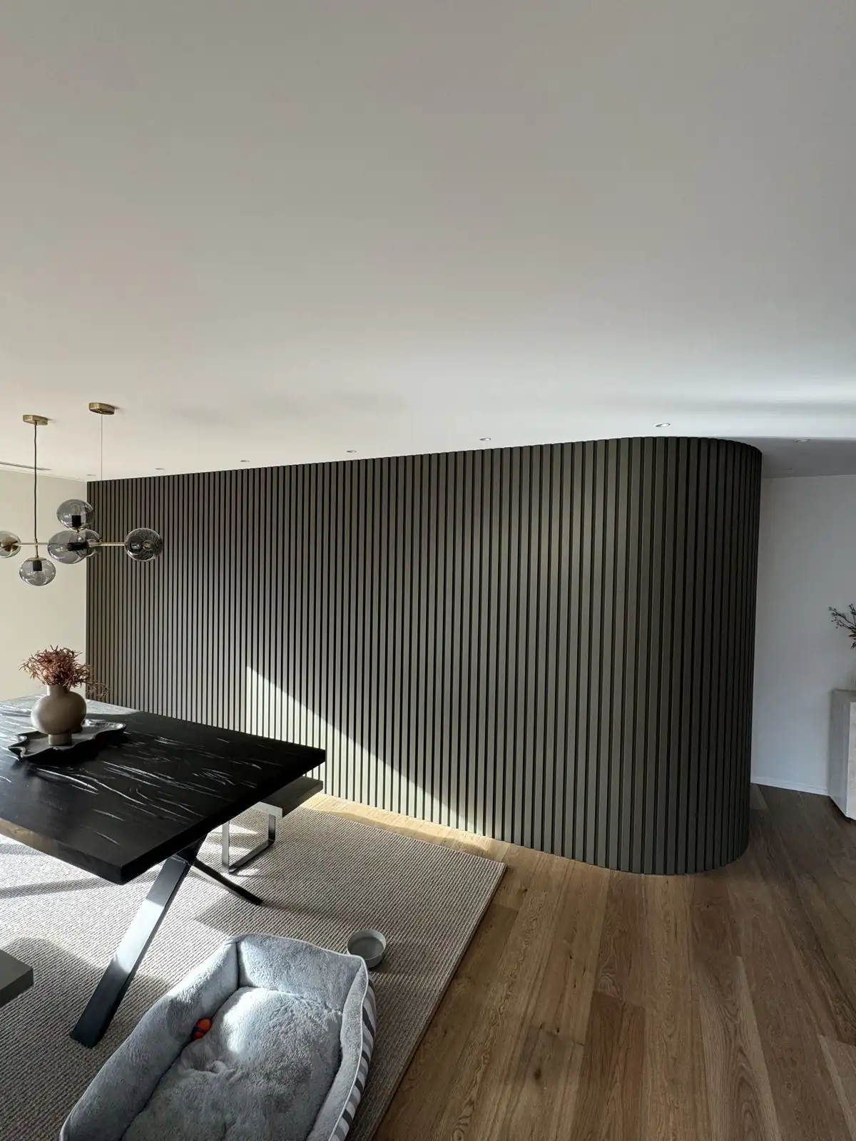 Dining area with a curved, dark slatted feature wall and timber floors on Erin Crescent, Mairehau
