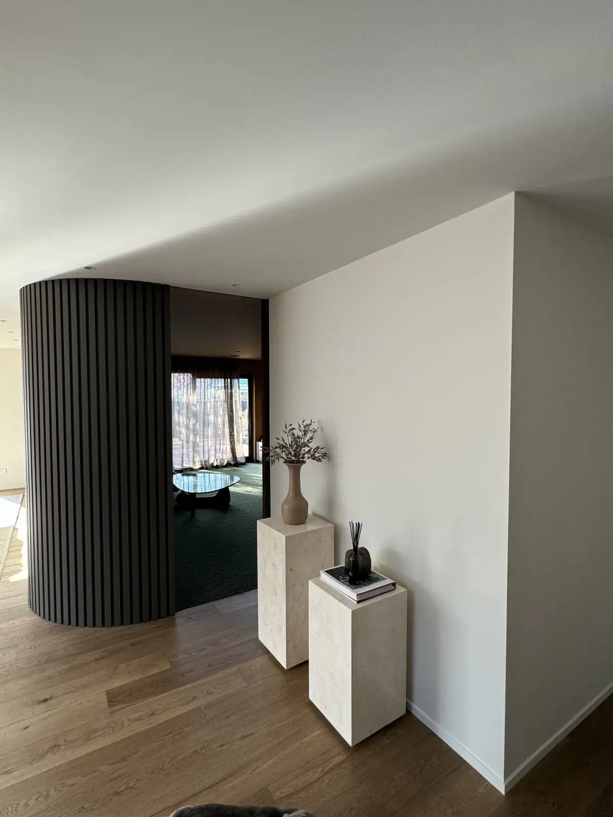 Curved slatted wall meeting the white plaster in the entry