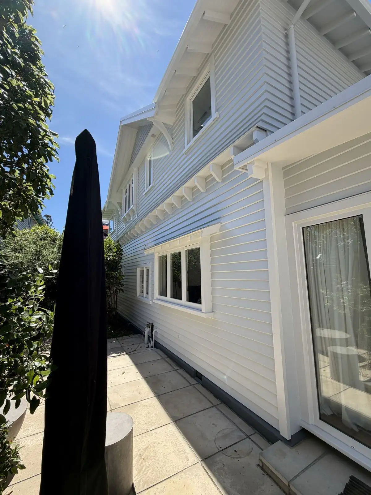 Freshly painted white weatherboard home on Marriner Street, Sumner, seen from the side courtyard