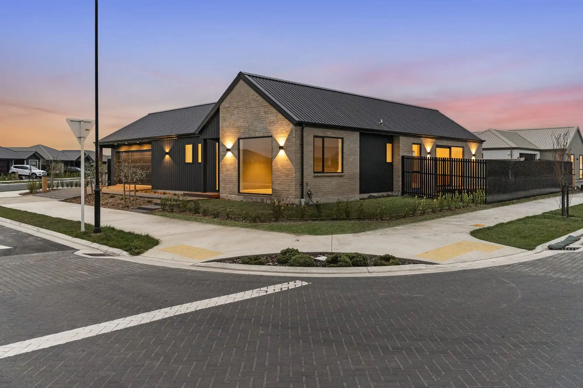 New single-storey home on Silvergrass Way, Rolleston, with dark cladding and brick, lit up at dusk