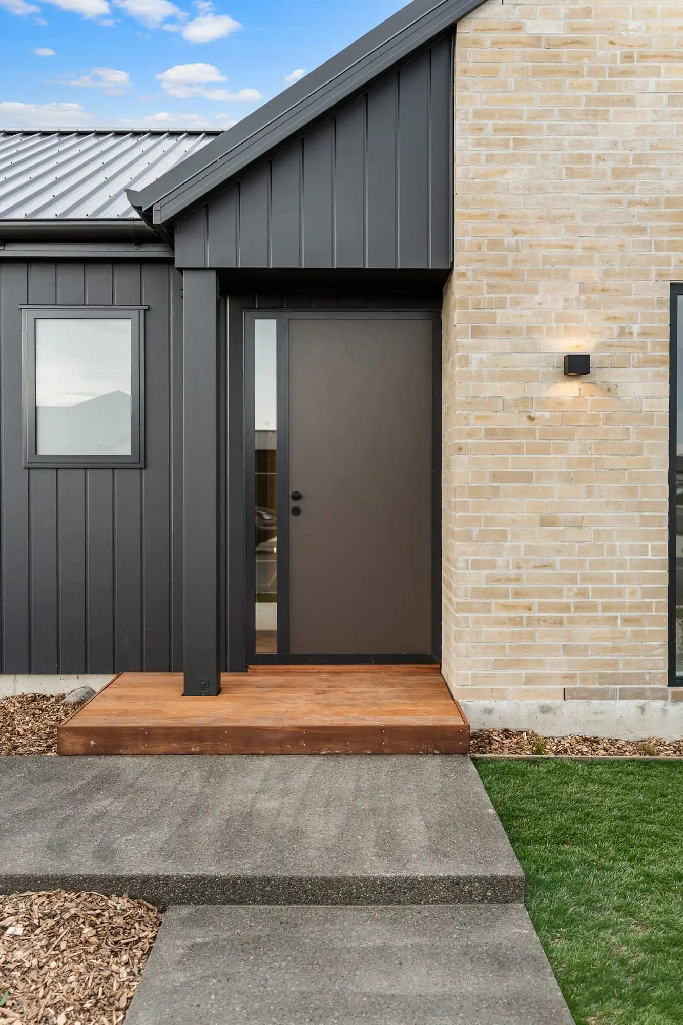 Front entry with dark vertical cladding, brick and a timber step